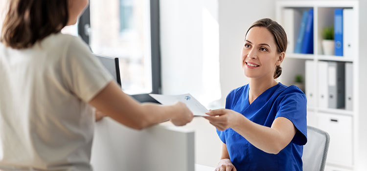 medical assistant takes paperwork from patient at front desk