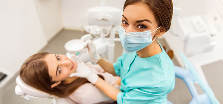masked dental assistant cleans patient teeth