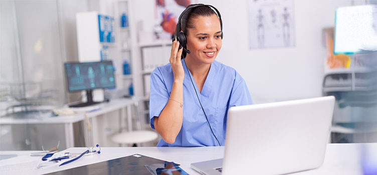 medical office administrator works on her laptop and talks to a patient through a headset
