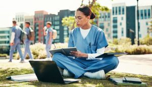 medical assistant student sits in the grass on campus working on homework