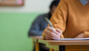 a person takes an exam at a desk with another exam taker in the background