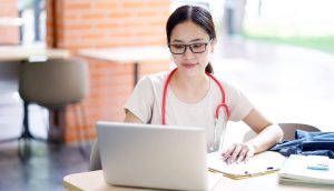 smiling female college student on laptop at table wearing a red stethoscope
