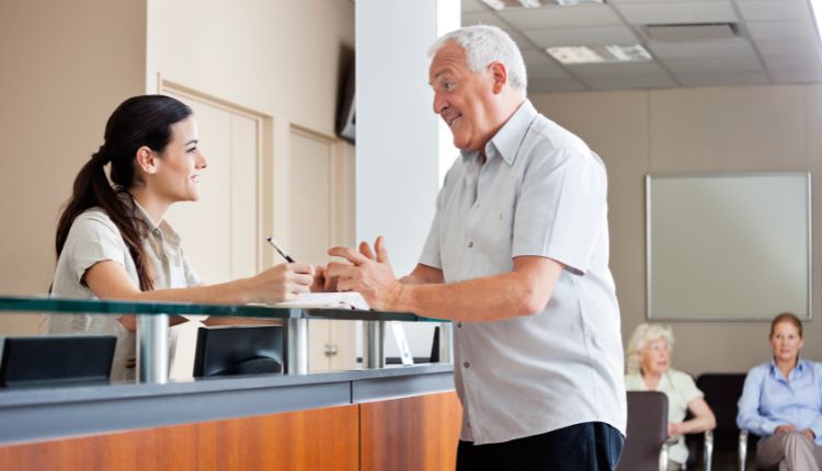 a medical assistant speaks with a patient at the front desk of a medical office